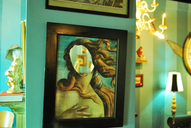 Mirror reflecting the Birth of Venus painting with the viewer's face as Venus, displayed at Amélie's French Bakery in North Carolina